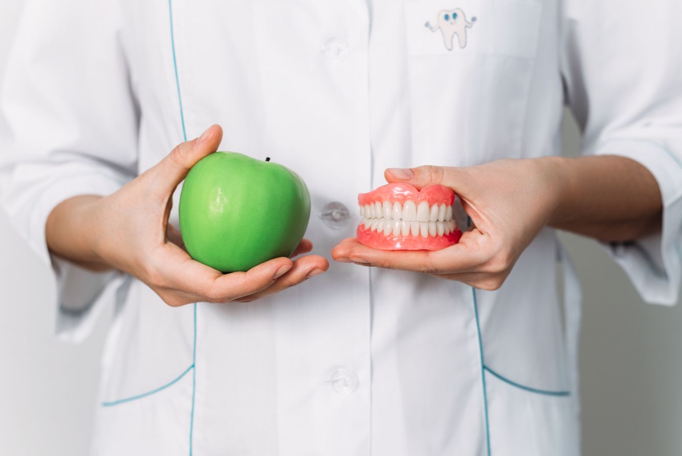 dentist holding dentures and apple lemont dental clinic