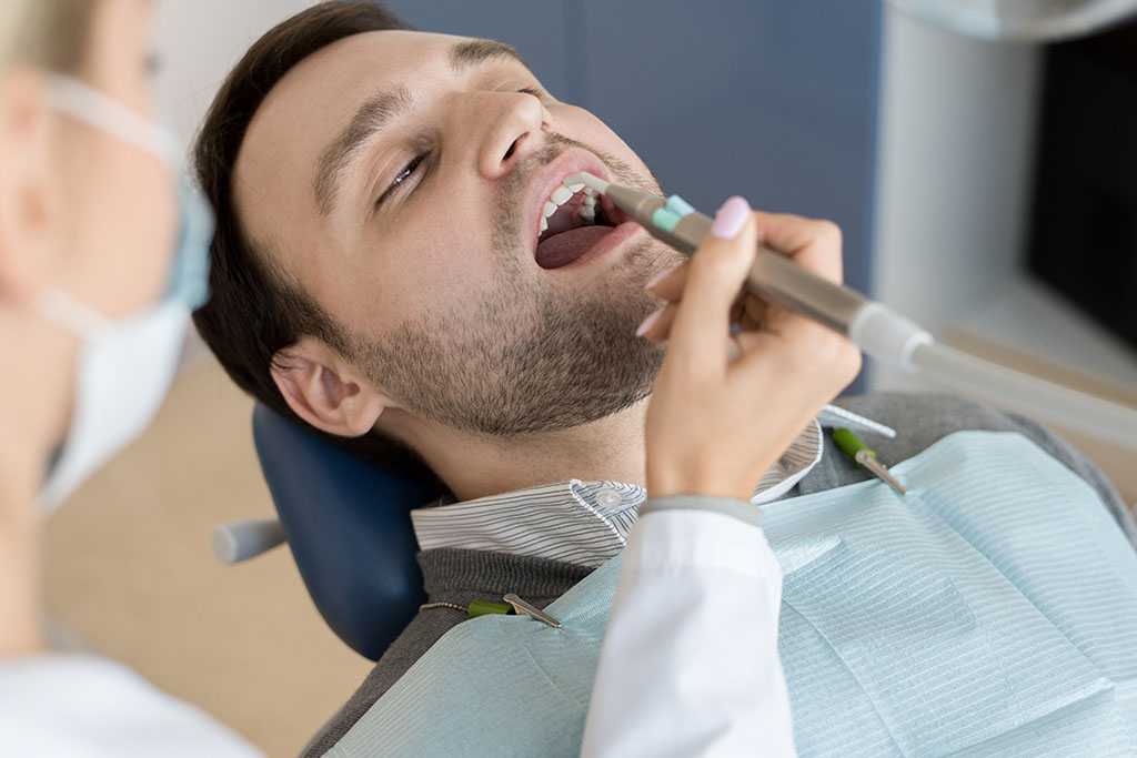 Portrait of mature man sitting in dental chair with mouth open while female dentist treating teeth in modern clinic, what does a cavity feel like